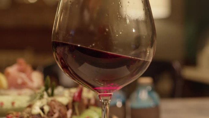 将红酒从瓶中倒入餐厅内的玻璃杯或高脚杯中的慢动作。红酒的特写在玻璃中形成美丽的波浪。在红色史诗电影相