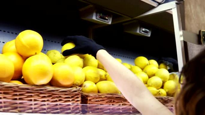 近距离的女工人在黑色手套stocking在超市的柠檬。年轻员工在工作。卷曲的女性安排在架子上的柠檬。