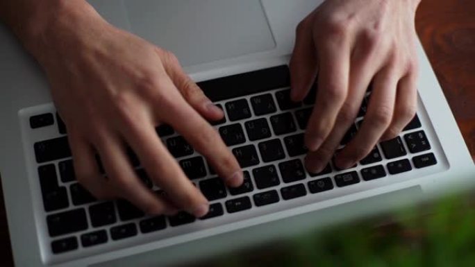 男士双手在桌子上笔记本电脑键盘上打字的特写镜头。