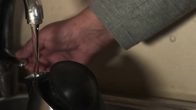 一名男子在电热水壶中装满了煮咖啡的水。厨房用具。