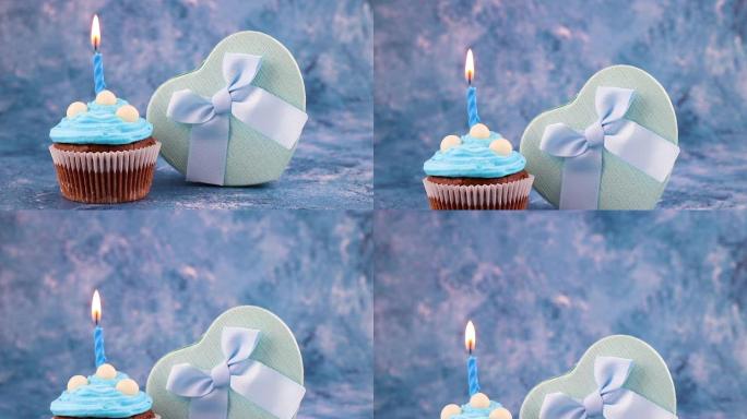 生日派对美味的巧克力杯蛋糕装饰蓝色奶油和蓝色背景蜡烛，带礼物