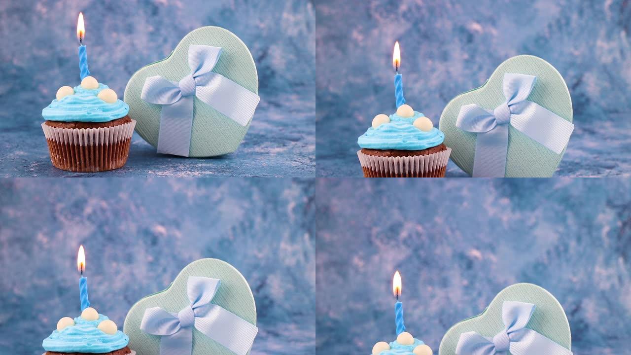 生日派对美味的巧克力杯蛋糕装饰蓝色奶油和蓝色背景蜡烛，带礼物