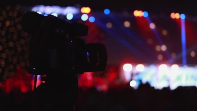 慢动作，人们聚会的剪影，摄像师在大厅的舞台前录制视频摇滚音乐会。彩色蓝色舞台灯光，带led灯的舞台聚