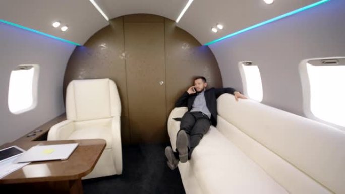 年轻人的肖像首席银行家董事在私人飞机上的电话交谈中躺在沙发上