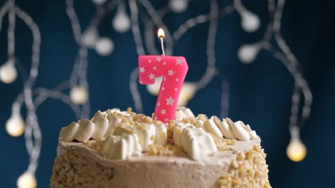 蓝色背景上有7号粉色蜡烛的生日蛋糕。蜡烛着火了。慢动作和特写视图