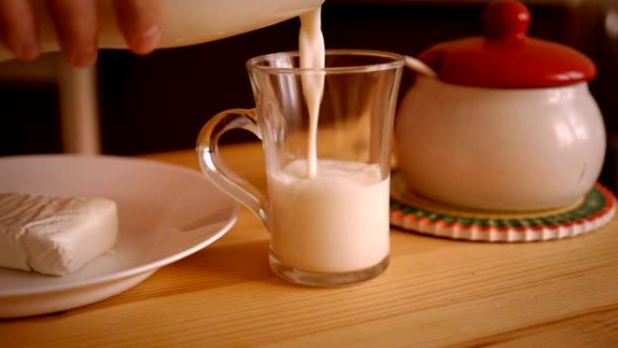 一个人将牛奶倒入木桌上的玻璃杯中。盘子里的奶酪。慢动作。