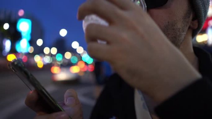 亚洲男子使用智能手机，在街头城市喝啤酒，舔嘴唇，伸出舌头，舔嘴唇