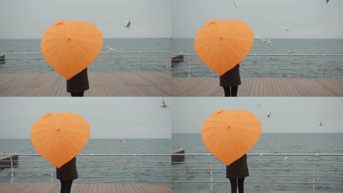 穿着橙色雨伞的女人在心形享受海鸥的海景