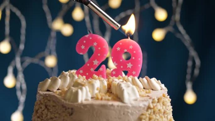 蓝色背景上有29号粉色蜡烛的生日蛋糕。蜡烛着火了。慢动作和特写视图