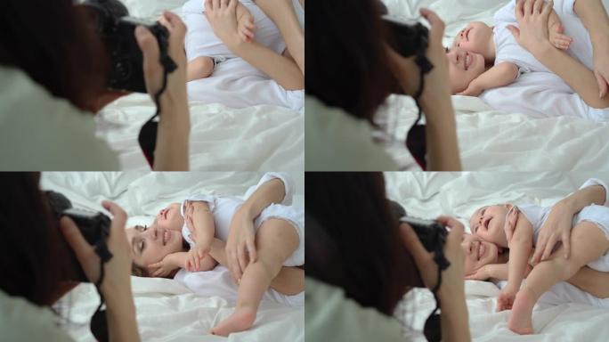 年轻的妈妈在拍照时在床上玩耍和拥抱婴儿