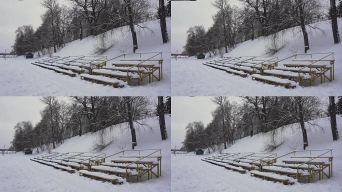白雪皑皑的长椅在冬天的夏季海滩上，白天在河边。季。白雪覆盖的观众看台