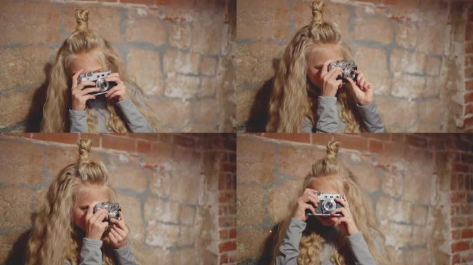 美丽的女孩在砖墙背景上的老式相机上拍照。时髦女孩使用复古相机在砖工作室拍照。