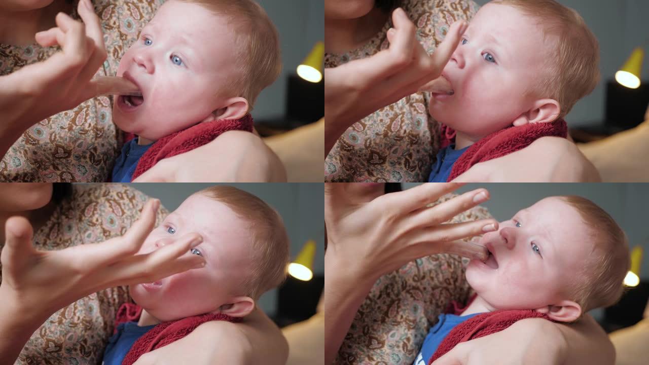 妈妈用戴在手指和口香糖凝胶上的牙刷按摩器按摩婴儿的牙龈。出牙概念。慢动作和特写