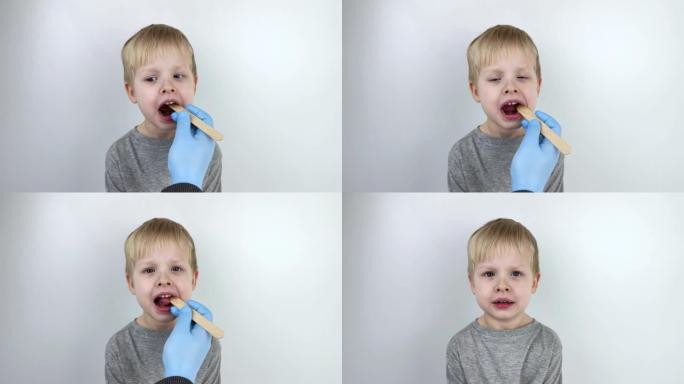 耳鼻喉科医生用木铲检查孩子的喉咙。可能的诊断是咽部，扁桃体或咽炎的炎症。