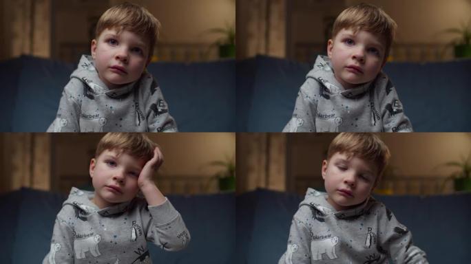 坐在家里沙发上的年轻心烦意乱的男孩的肖像。悲伤的孩子的脸看着镜头慢动作。
