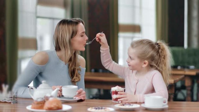 充满爱心的顽皮女儿用鲜奶油喂养微笑的母亲甜点。红色相机上的中等镜头