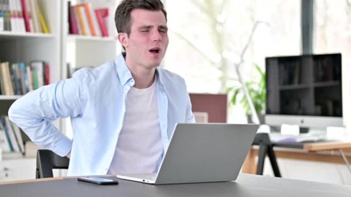 背部疼痛的年轻人在笔记本电脑上工作