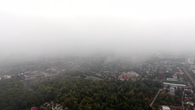 在低层云雾中的小镇无人机镜头。在雾云掠过的城市中拍摄的俯视图。云雾中的城市景观鸟瞰图