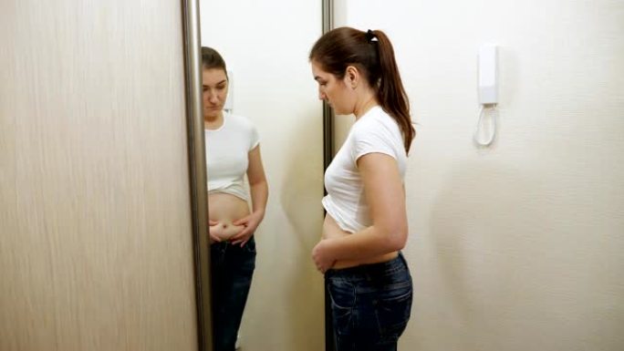 镜子前的年轻超重妇女触诊了她的侧面和腹部