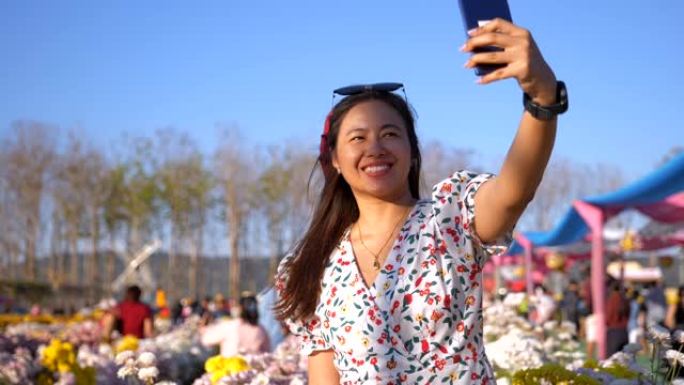 场景慢动作的快乐的亚洲女人放松和使用手机自拍的照片花在田野五颜六色的花