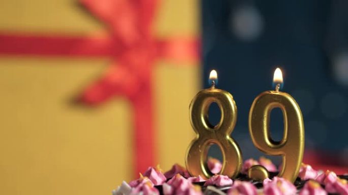 生日蛋糕89号点火器燃烧的金色蜡烛，蓝色背景礼物黄色盒子用红丝带绑起来。特写和慢动作