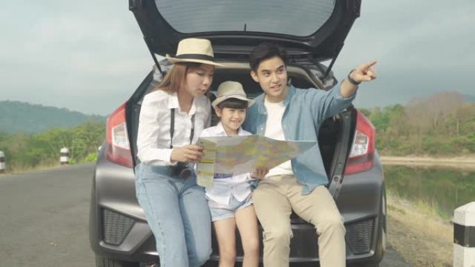 亚洲家庭的肖像坐在车里，父亲指着风景，母亲带着女儿在度假时一起看着美丽的风景，拿着地图。幸福的家庭时