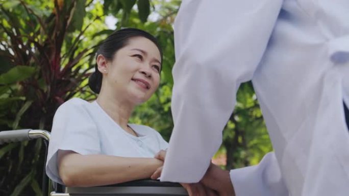 关爱之手，亚洲医生抱着花园背景的轮椅上的高级女性。快乐的微笑。