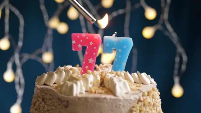 蓝色背景上有77号粉色蜡烛的生日蛋糕。蜡烛着火了。慢动作和特写视图