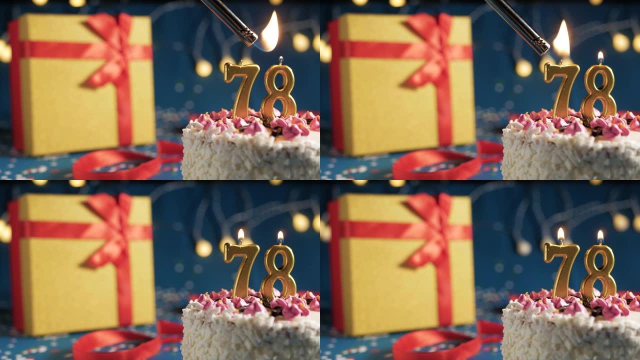 白色生日蛋糕编号78点灯燃烧的金色蜡烛，蓝色背景带灯和用红丝带绑起来的礼物黄色盒子。特写