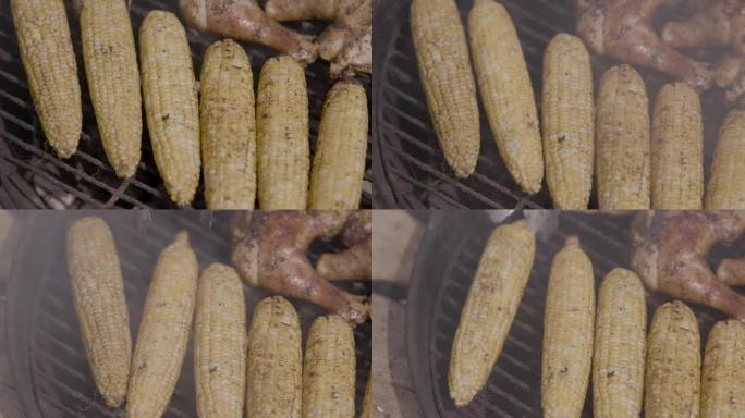 夏天在公园的木炭黑水壶烤架上在玉米棒上抽玉米和烧烤鸡腿。