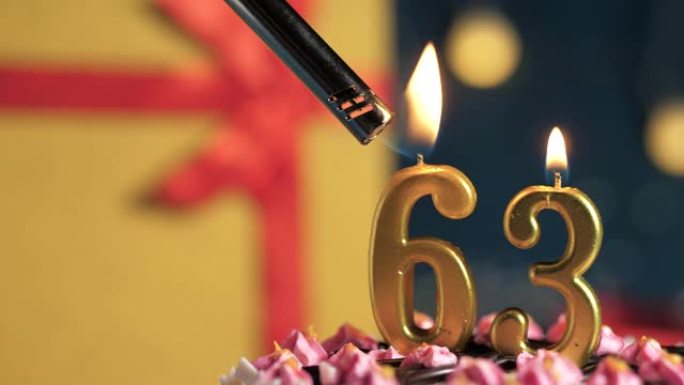 生日蛋糕编号63点灯燃烧的金色蜡烛，蓝色背景礼物黄色盒子用红丝带绑起来。特写和慢动作