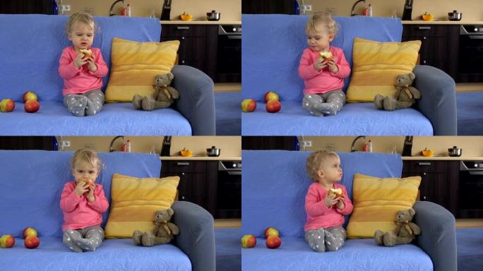 可爱的女婴坐在沙发上吃大苹果水果。