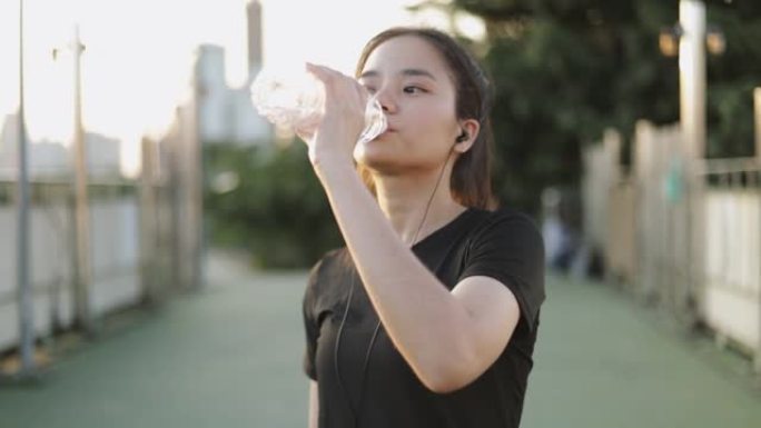 迷人的亚洲女性慢跑跑步后喝水。