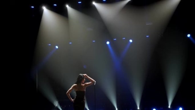一位美丽的歌手在蓝色聚光灯下在黑暗中的舞台上摆姿势。