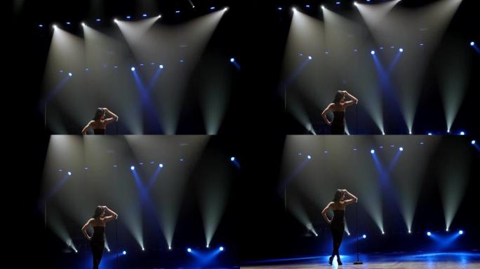 一位美丽的歌手在蓝色聚光灯下在黑暗中的舞台上摆姿势。
