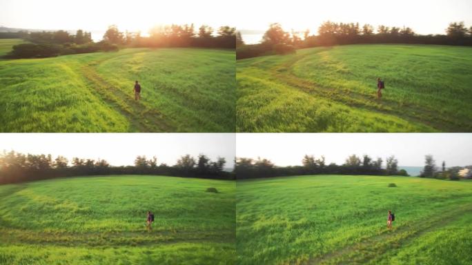 带着背包的男人在日落时分在草场上行走，无人机运动