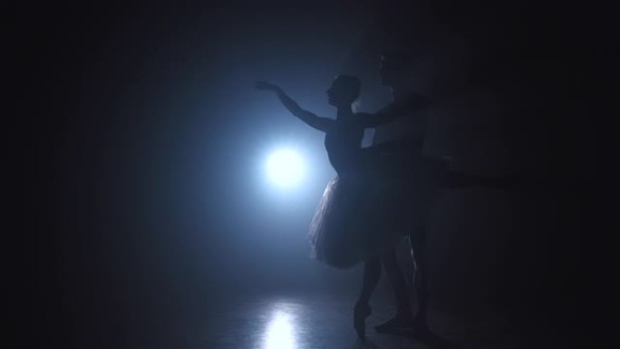 青年男子的剪影在与芭蕾舞女演员在黑暗的烟雾工作室与聚光灯练习古典芭蕾舞脚尖旋转。性感的舞。缓慢的运动