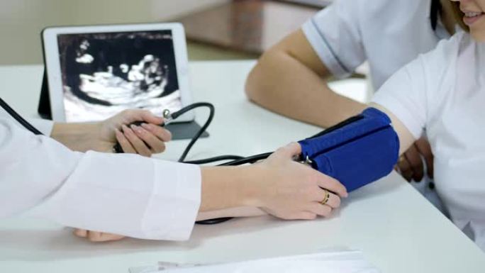 怀孕。医生用医用压力计测量血压并咨询年轻夫妇患者