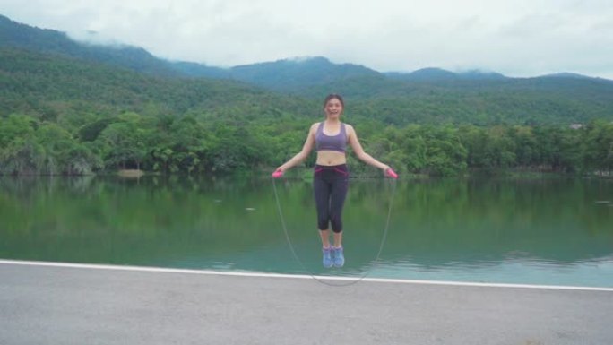 年轻健康快乐的亚洲女性在户外自然公园跳绳，湖光山景，健康的生活方式，慢动作