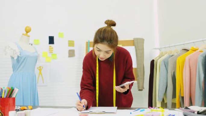 亚洲女性时装设计师在工作室工作时使用智能手机，工作场所，亚洲小企业概念