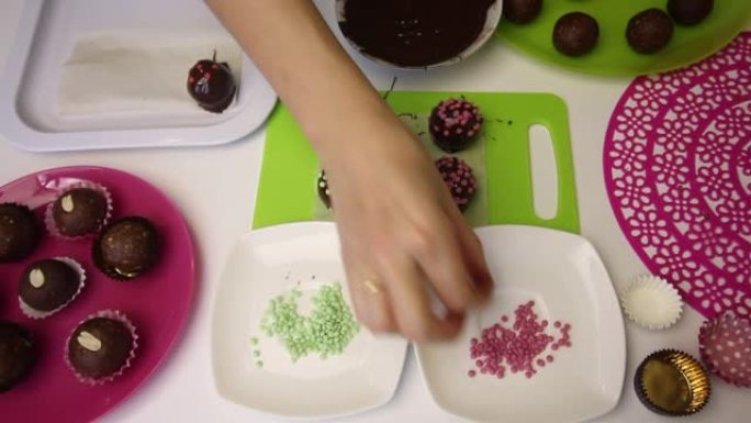 一个女人装饰着撒上巧克力球。做一个土豆蛋糕。盘子旁边是蛋糕坯料，液体巧克力和彩色洒。