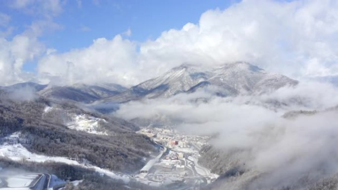 雪山覆盖林地之间的冬季城市景观。鸟瞰图冬季山谷的雪城。无人机在山谷的冬季高地上查看蓝天和云