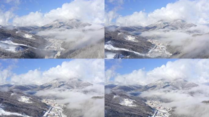 雪山覆盖林地之间的冬季城市景观。鸟瞰图冬季山谷的雪城。无人机在山谷的冬季高地上查看蓝天和云