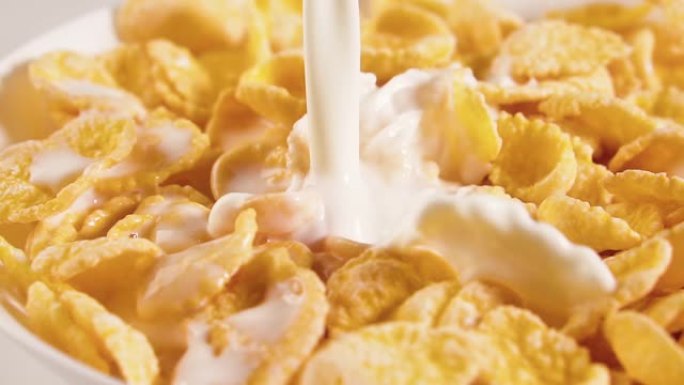 牛奶倒入碗玉米片中，慢动作。健康的牛奶麦片早餐，特写。