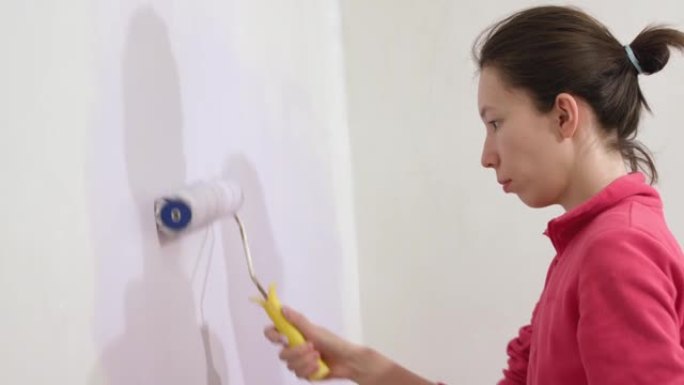 年轻的亚洲幸福女人在新房子里用油漆滚筒画内墙