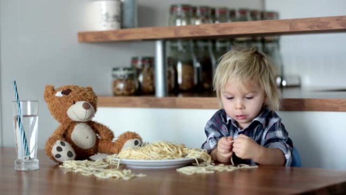 小男孩，蹒跚学步的孩子，午餐吃意大利面，做喂养泰迪熊的朋友