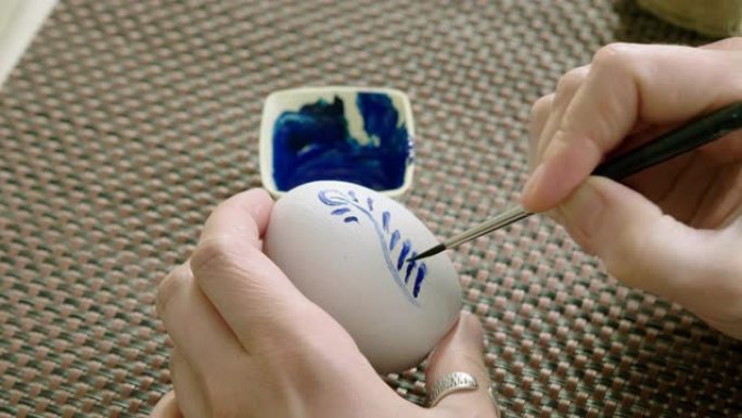 复活节假期。女人在鸡蛋蛋壳上涂上蓝色花卉图案，涂上白色油漆。4K