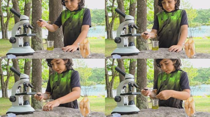 在阳光明媚的夏日，在湖岸的户外，用显微镜工作的9岁男孩-准备标本，观察和学习自然。4K UHD视频片