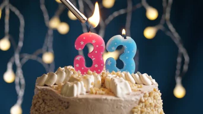蓝色背景上有33号粉色蜡烛的生日蛋糕。蜡烛着火了。慢动作和特写视图