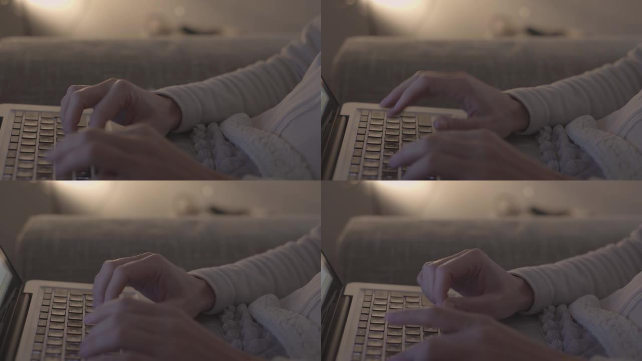 现代概念: 在柔和的灯光，无等级的现代氛围中，用手指敲击键盘，用笔记本电脑坐在沙发上的女人的手的特写